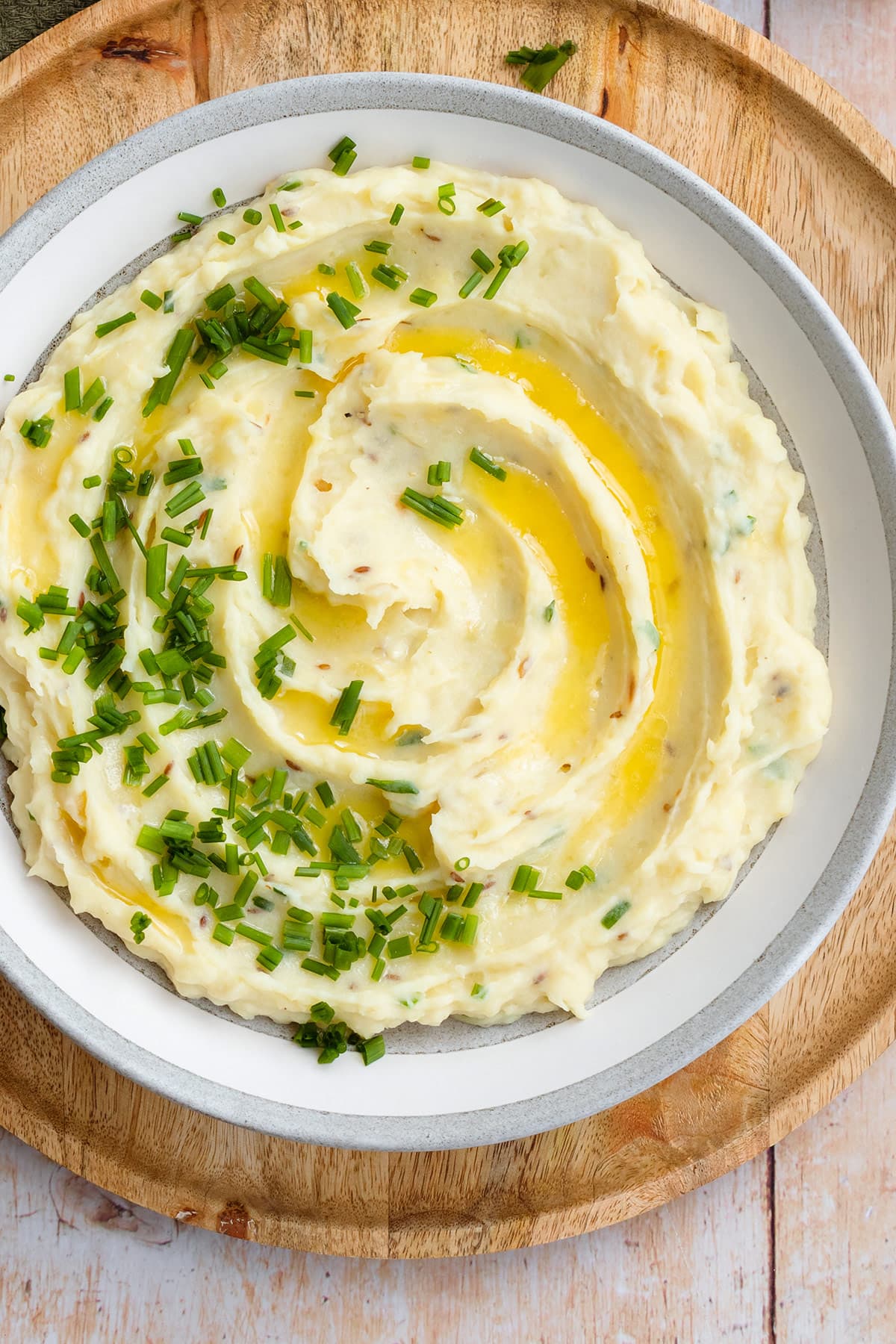 Mashed potatoes topped with fresh chives and butter in a grey shallow bowl.