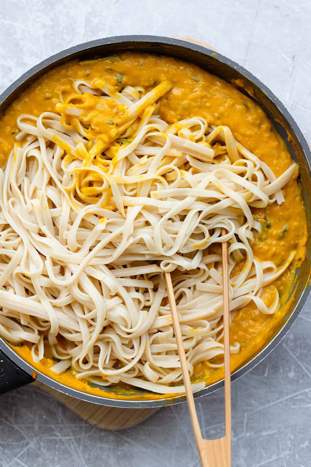 Fettucine being tossed with pumpkin sauce in a pan.