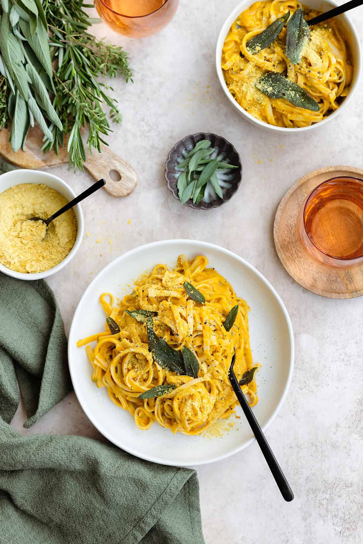 Pumpkin pasta topped with fried sage on a white plate with a black fork in the pasta.