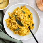 Pumpkin pasta topped with fried sage on a white plate with a black fork in the pasta.