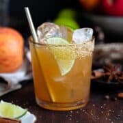 A cocktail in a short glass with a gold rim garnished with a lime slice on a dark wooden background.