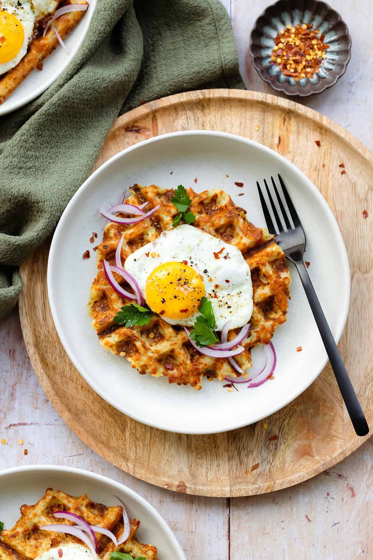 Waffles on a white plates with a sunny side up eggs on top and red onions.