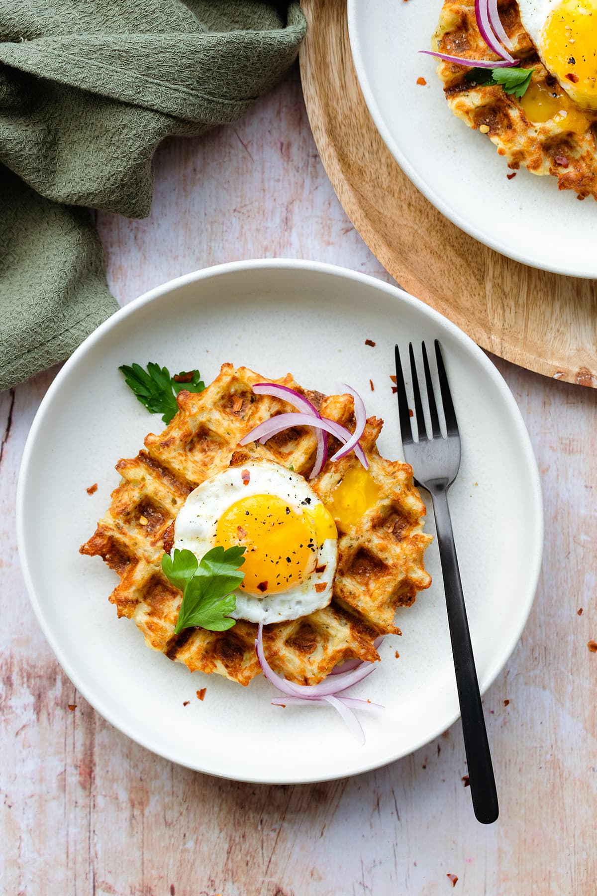 Waffles on a white plate with a sunny side up egg on top and red onions.