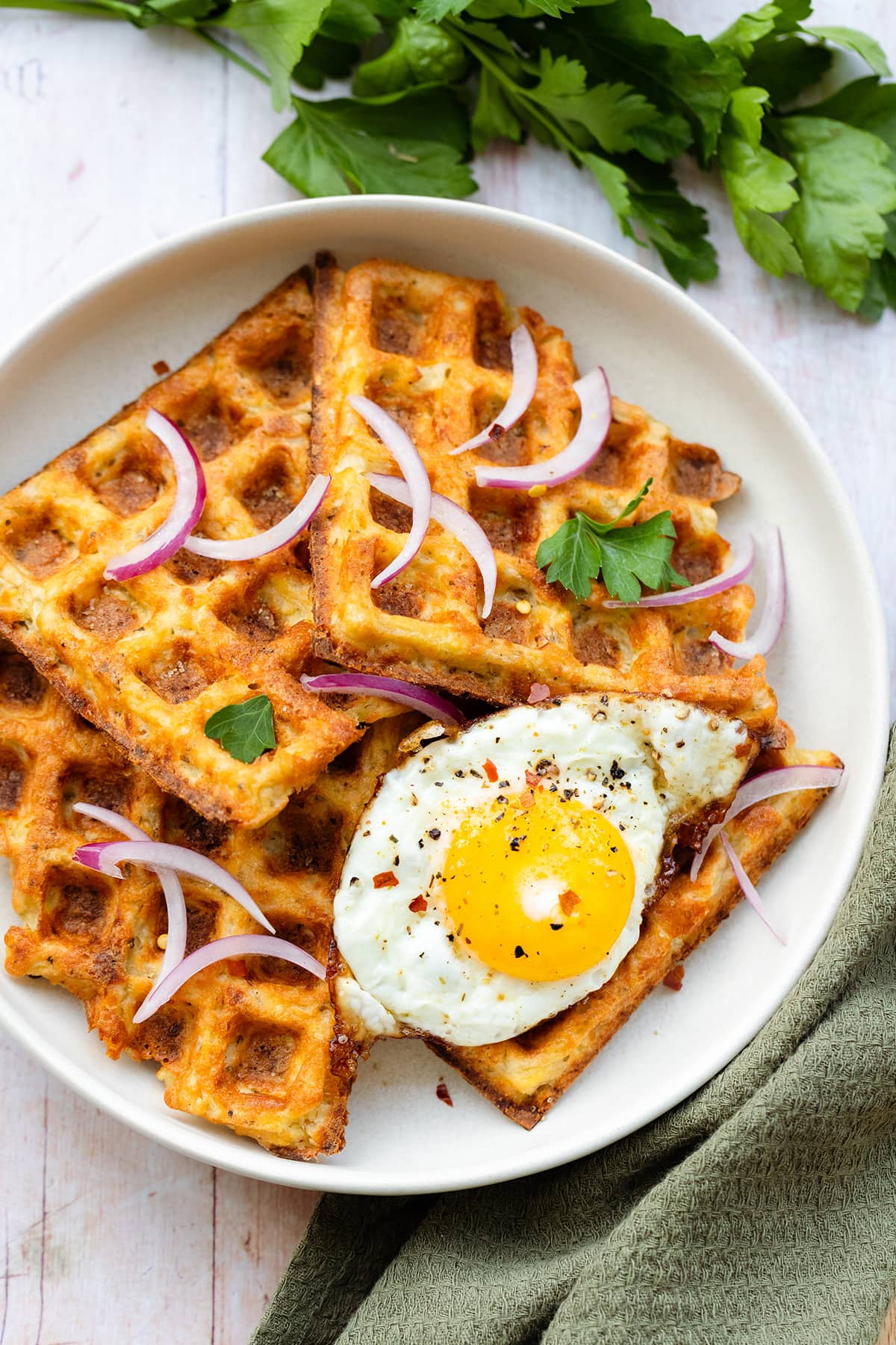 Four waffles on a white plate with a sunny side up egg on top and red onions.