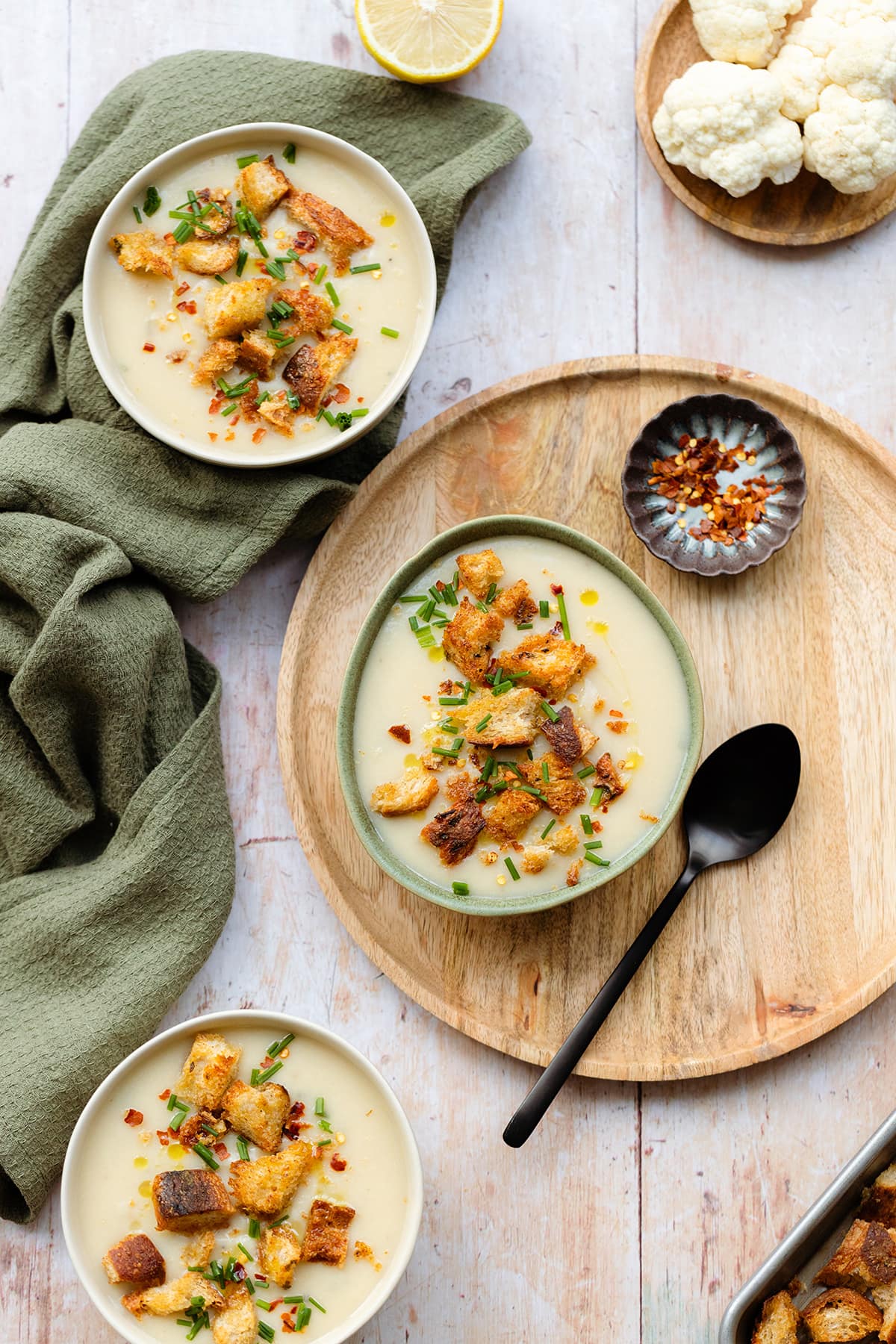 Cauliflower soup topped with croutons and fresh herbs in a white and green bowls on a wooden background.