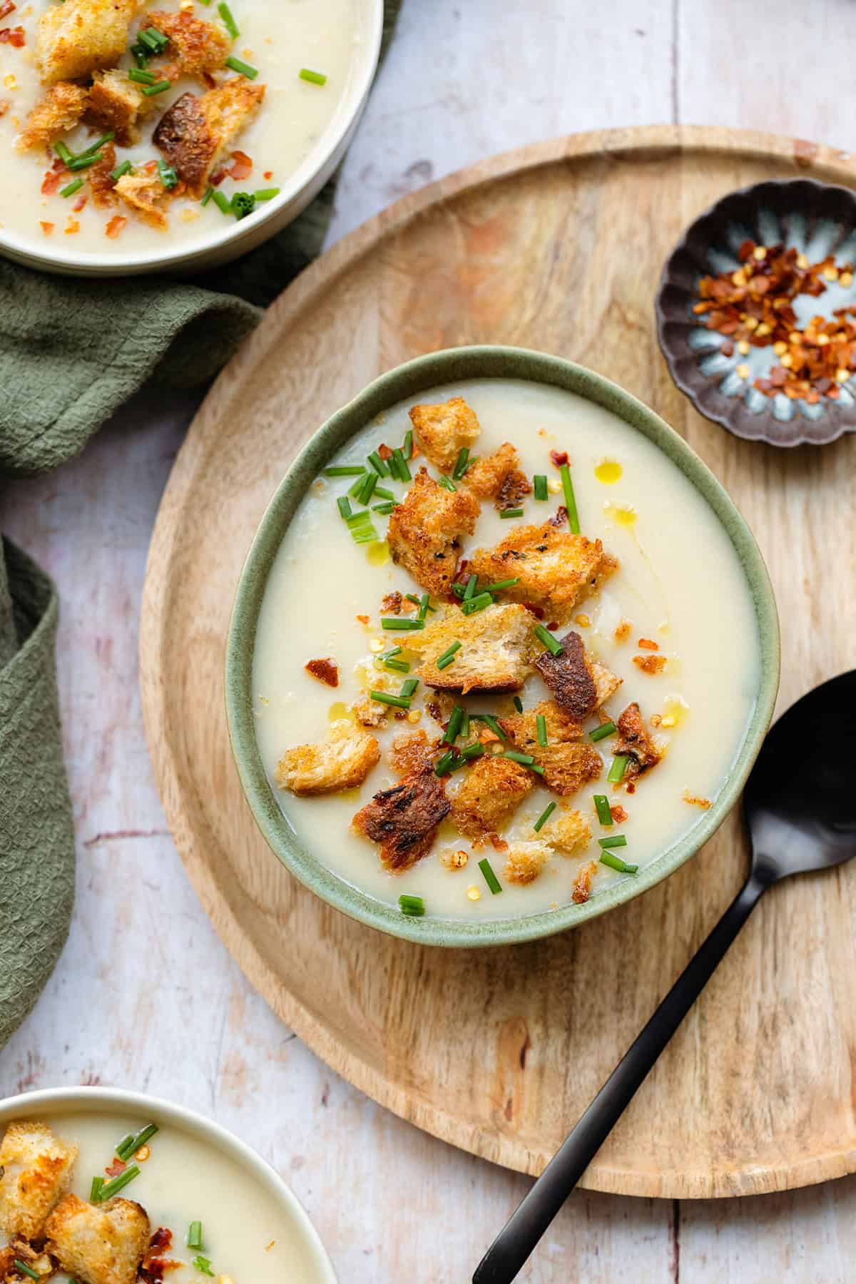 Cauliflower soup topped with croutons and fresh herbs in a white and green bowls on a wooden background.