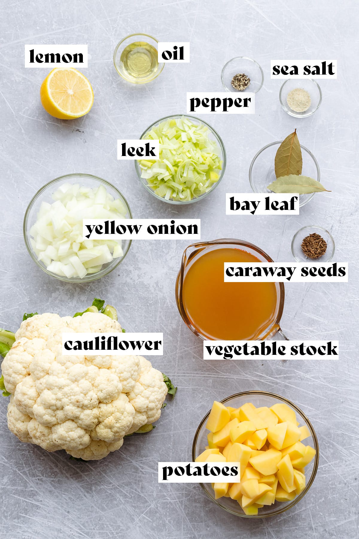 Ingredients for cauliflower soup all laid out on a scratched metal background.