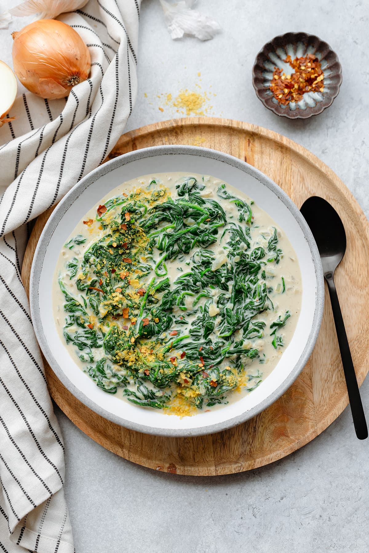 Creamy spinach served on a grey ceramic bowl sprinkled with nutritional yeast and chili flakes.