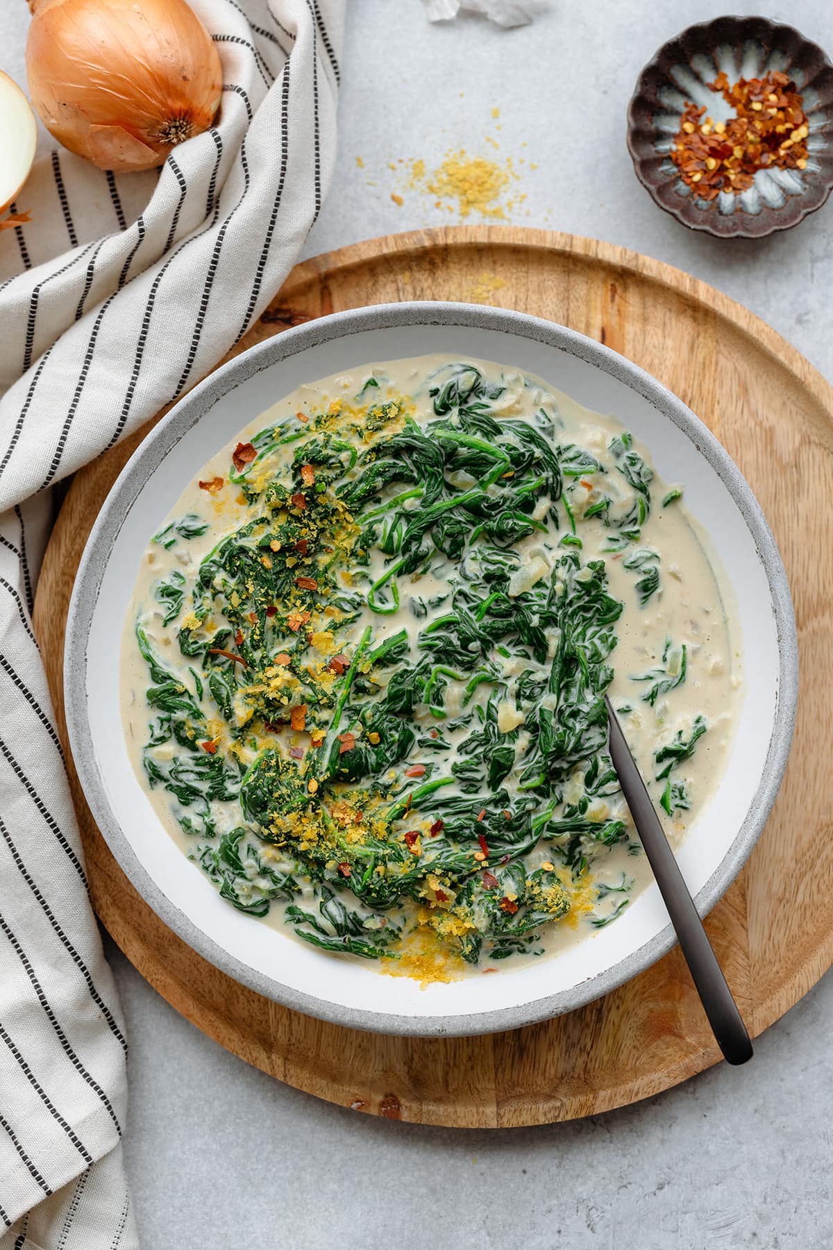Creamy spinach served on a grey white ceramic plate sprinkled with nutritional yeast and chili flakes.