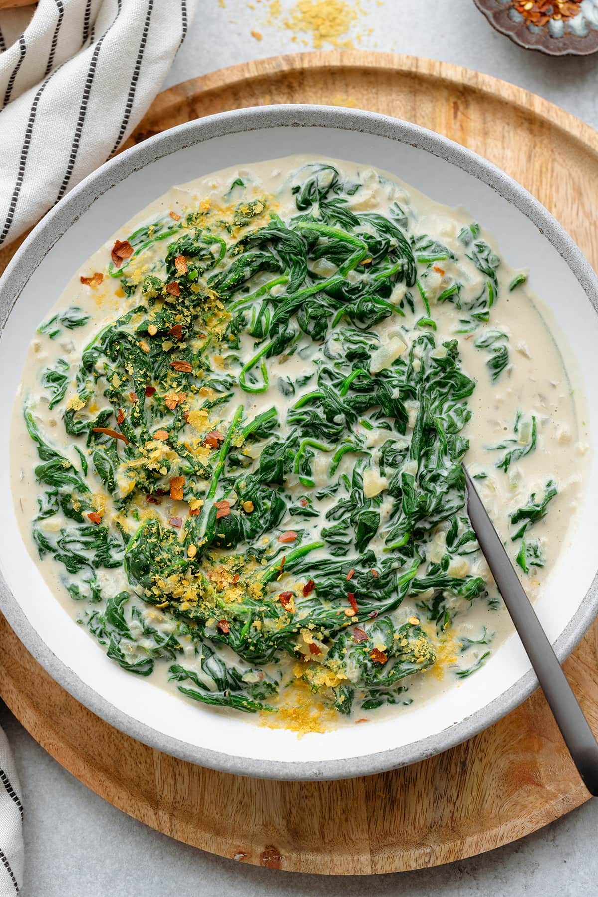 Creamy spinach served on a grey white ceramic plate sprinkled with nutritional yeast and chili flakes.