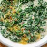 A close up of Creamed spinach on a grey ceramic bowl sprinkled with nutritional yeast and chili flakes.