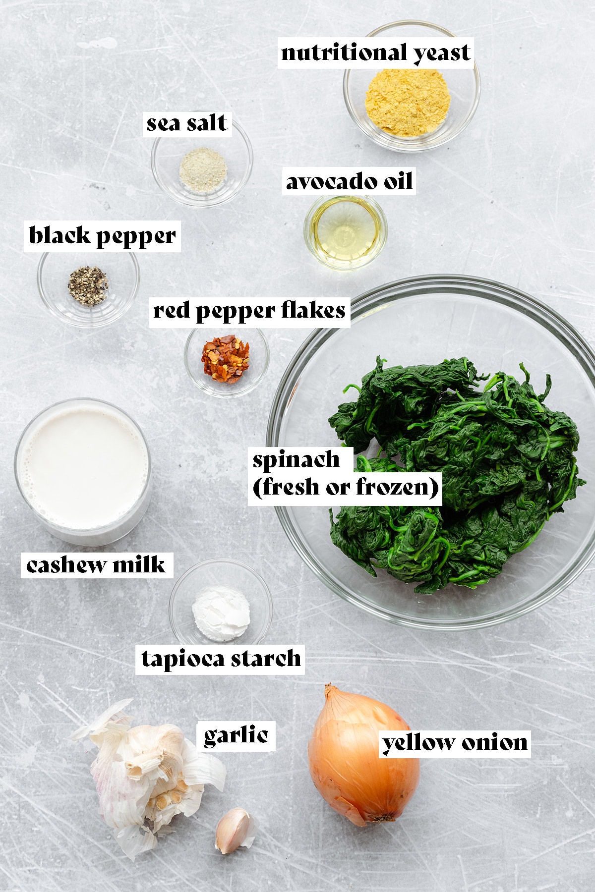 Ingtredients for vegan creamed spinach laid out on a scratched metal background.