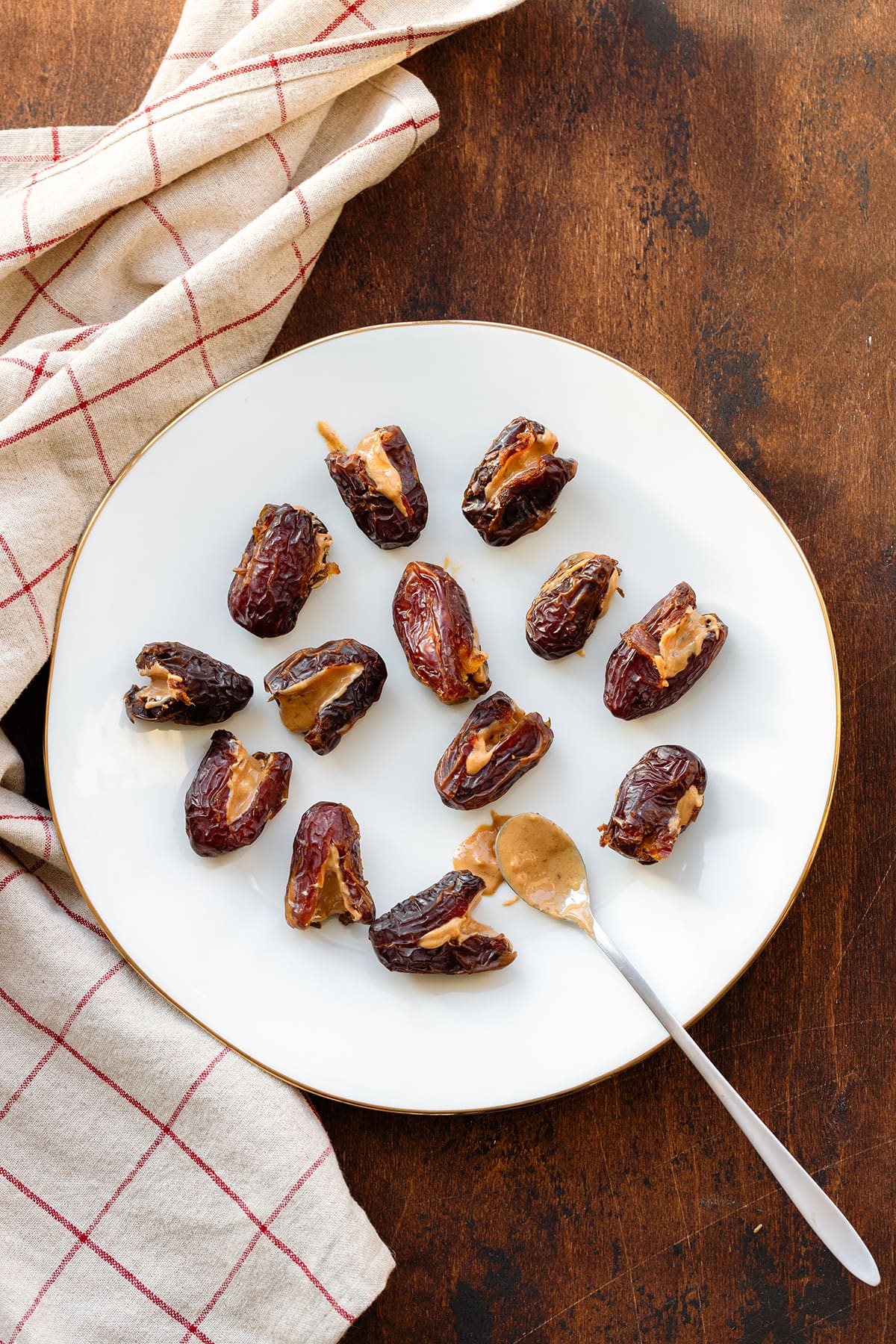 Medjool dates stuffed with peanut butter on a white plate and a dark wooden background.