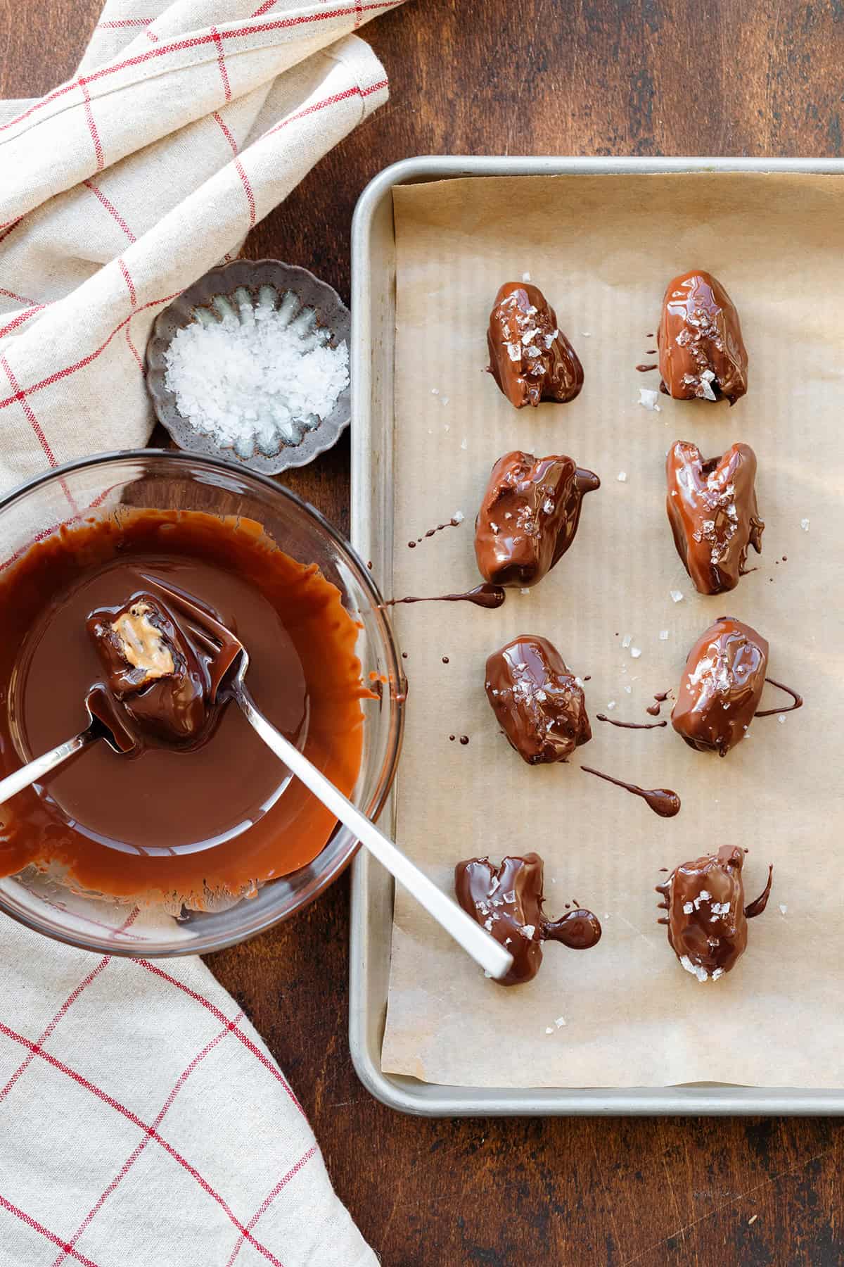 Freshly chocolate covered dates sprinkled with sea salt on a baking sheet.