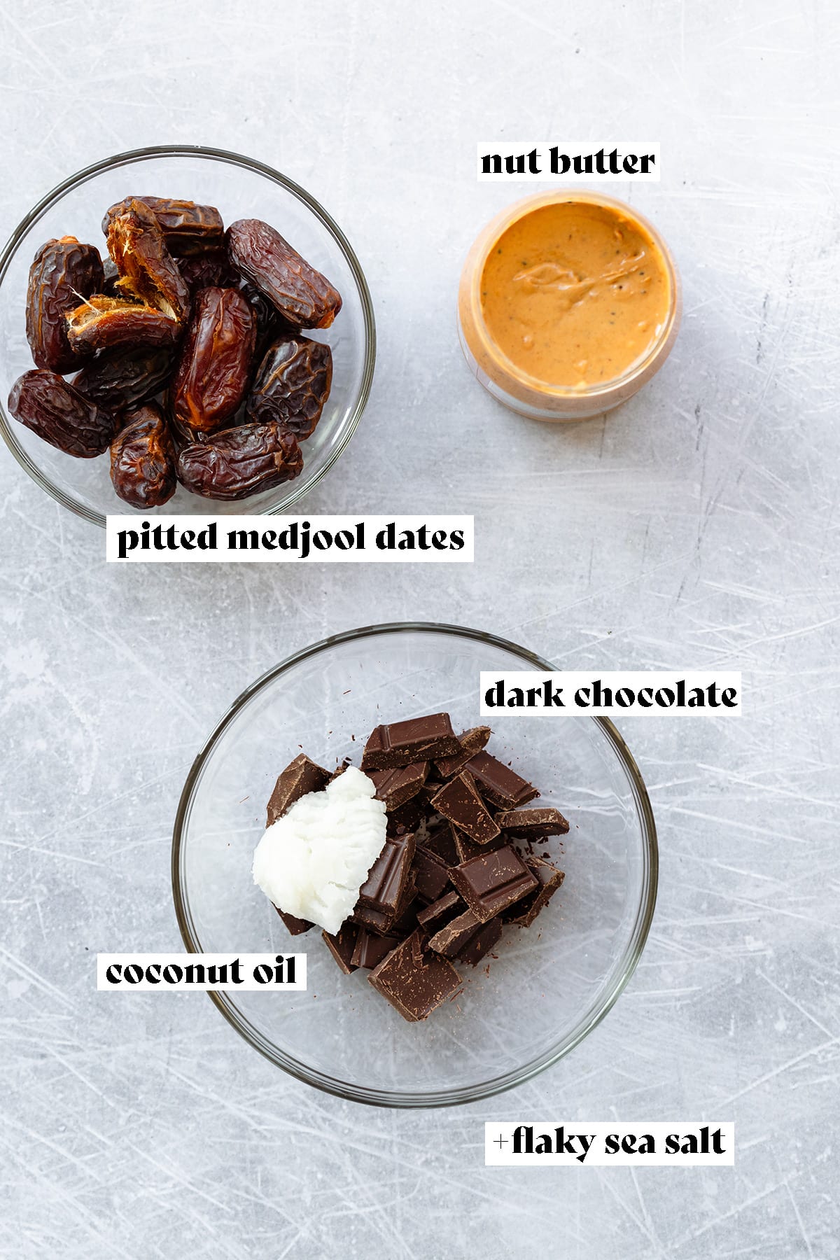 Dates, chocolate, coconut oil, and peanut butter laid out on a scratched metal surface.