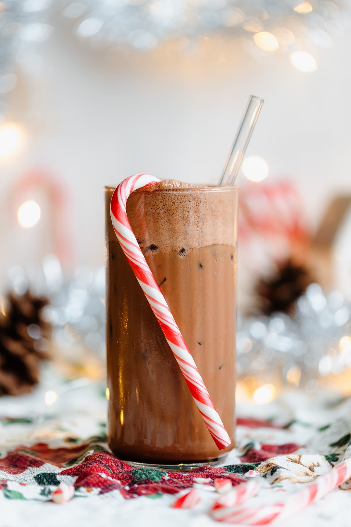 Iced peppermint mocha in a tall glass with a straw and a candy cane hanging on the rim.