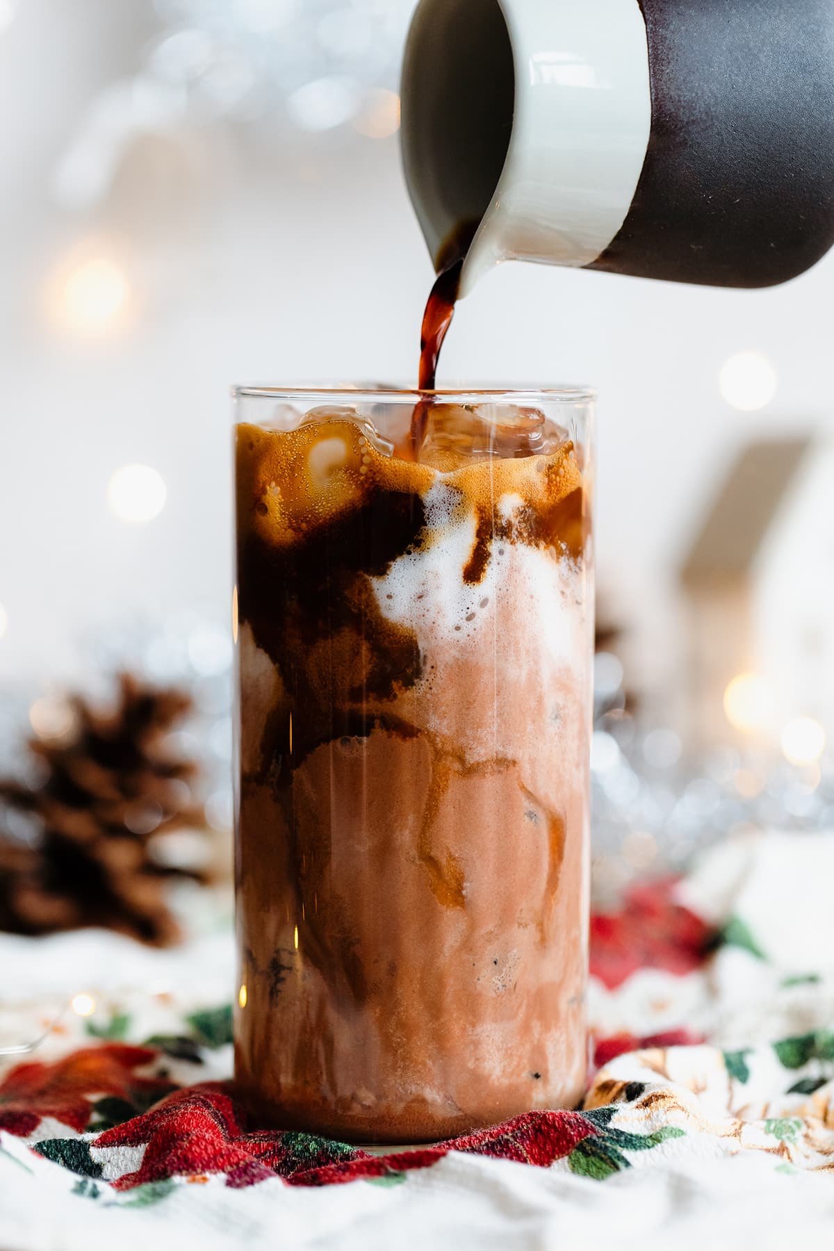 Chocolate milk and ice in a tall glass with espresso being poured over it.