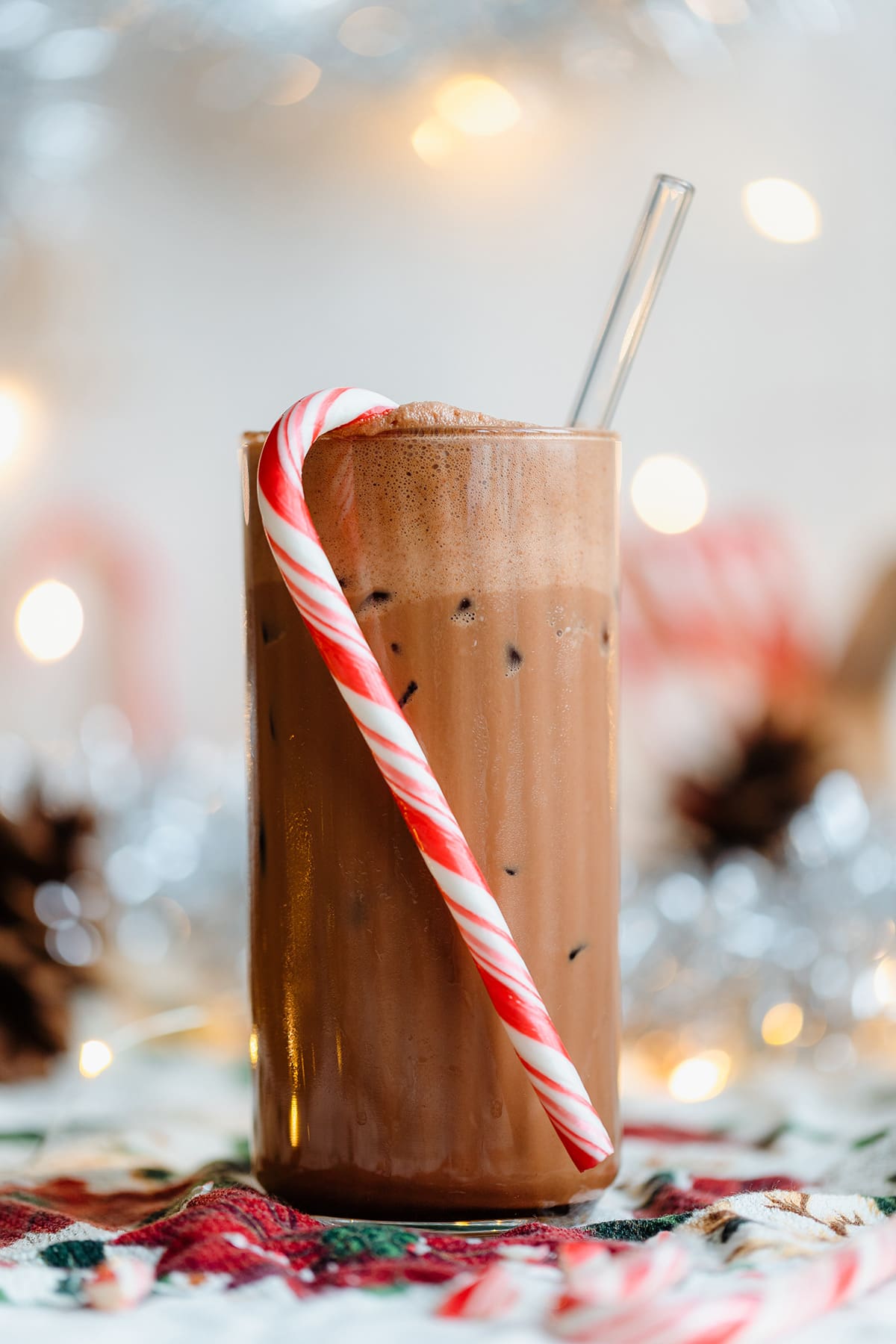 Iced mocha in a tall glass with a straw and a candy cane hanging on the rim.