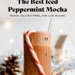 Iced peppermint mocha in a tall glass with a straw and a candy cane hanging on the rim.