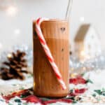 Iced mocha in a tall glass with a straw and a candy cane hanging on the rim.