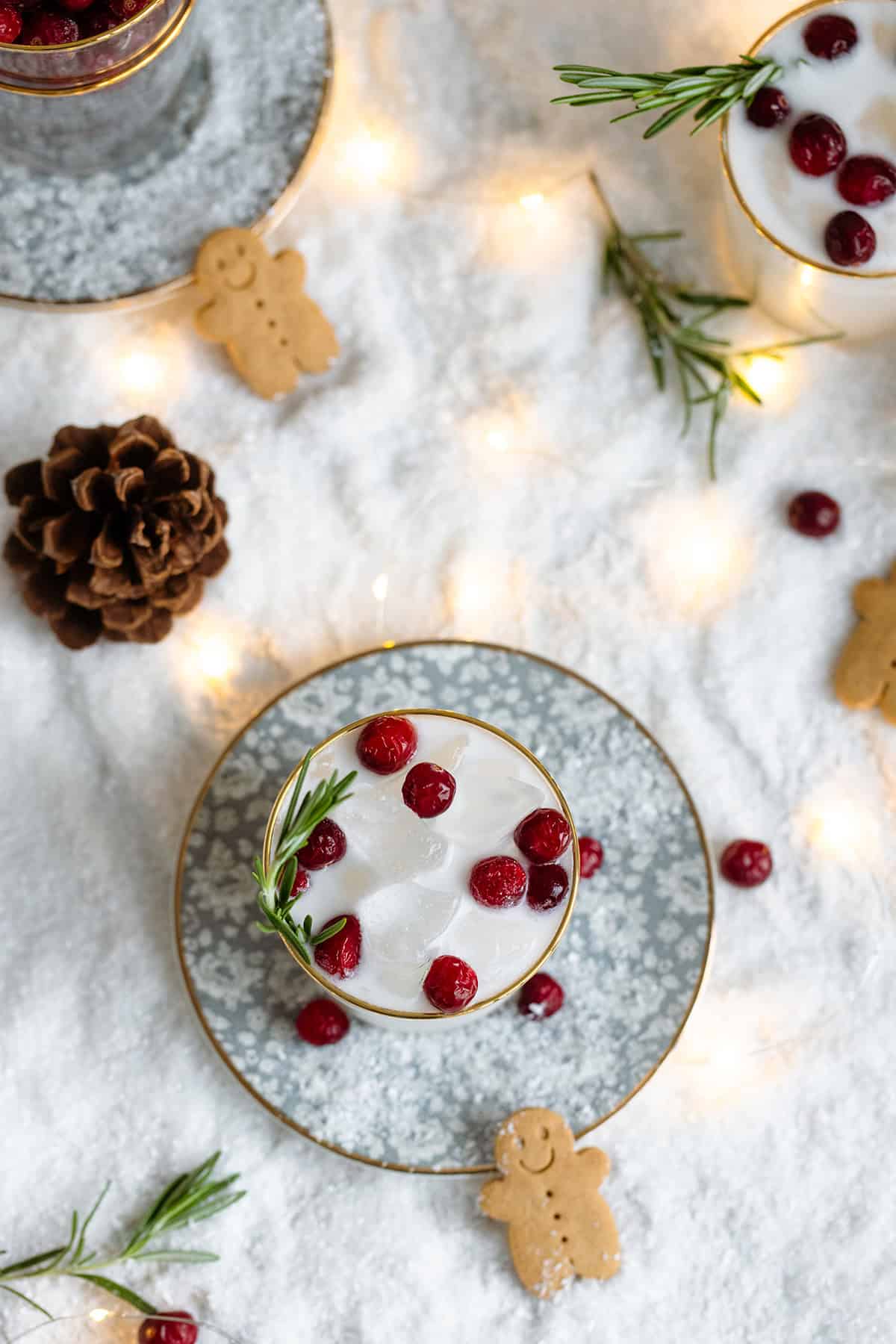 White margarita in a short glass with a gold rim, garnished with fresh cranberries, and rosemary spring.