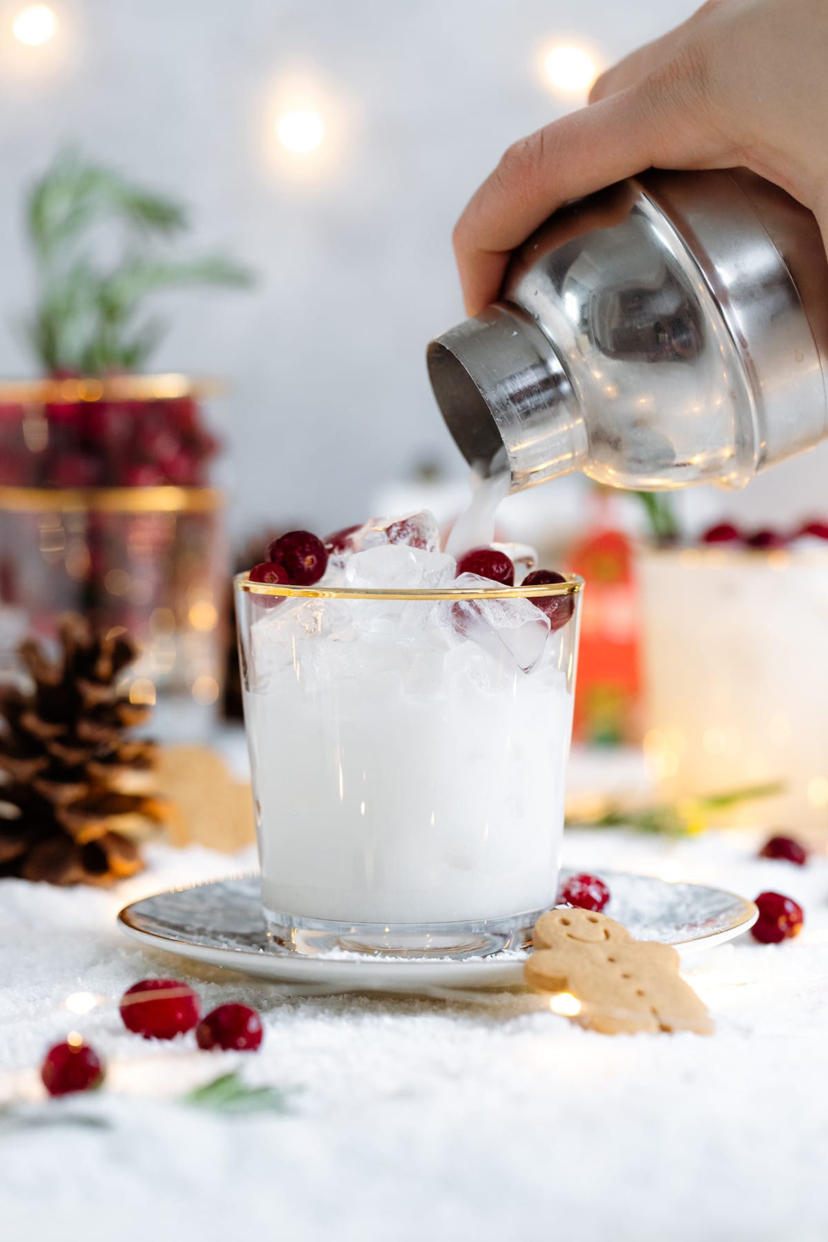 White margarita being poured in a short glass with a gold rim, christmas decorations are around.