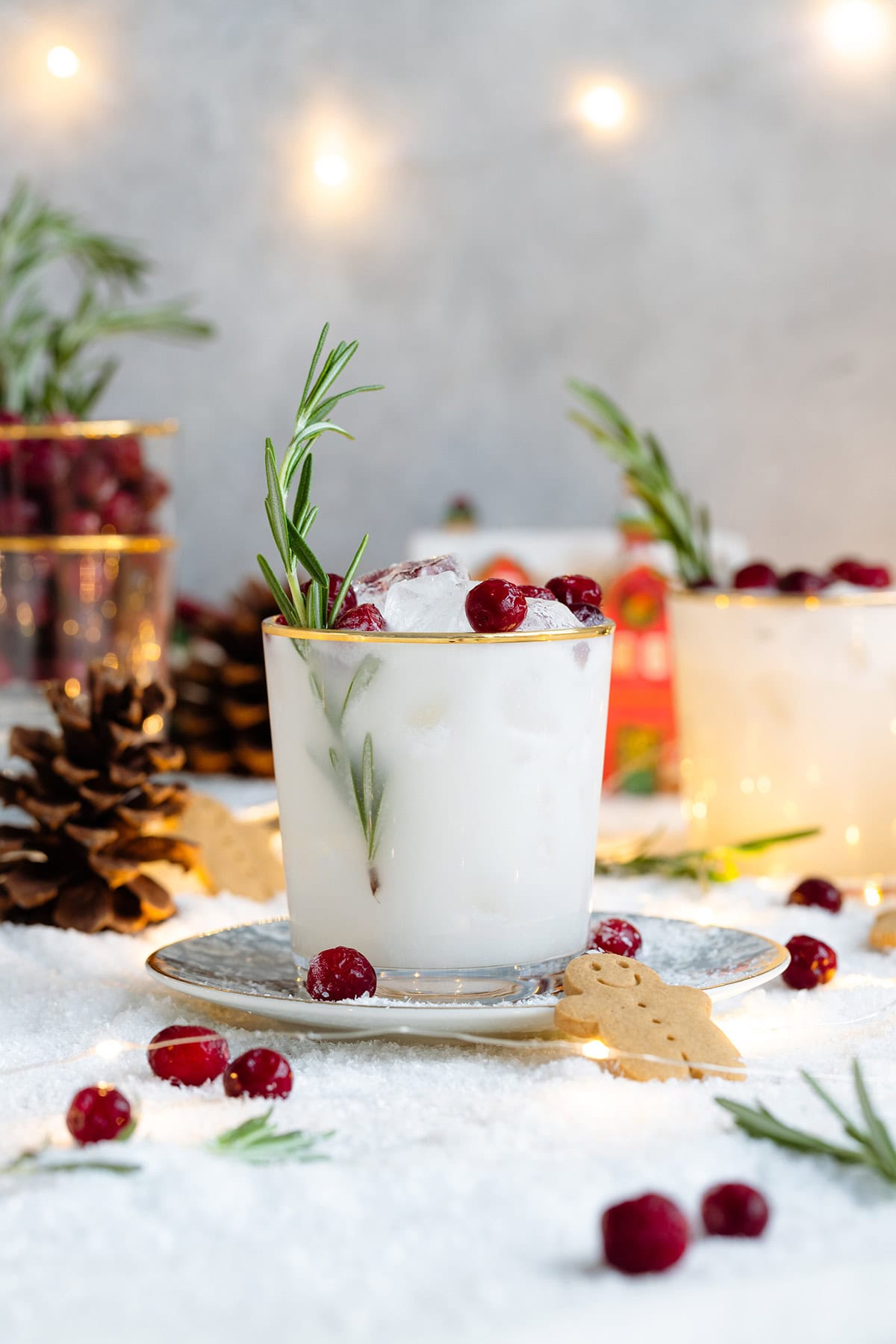 White margarita in a short glass with a gold rim, garnished with fresh cranberries, and rosemary spring.