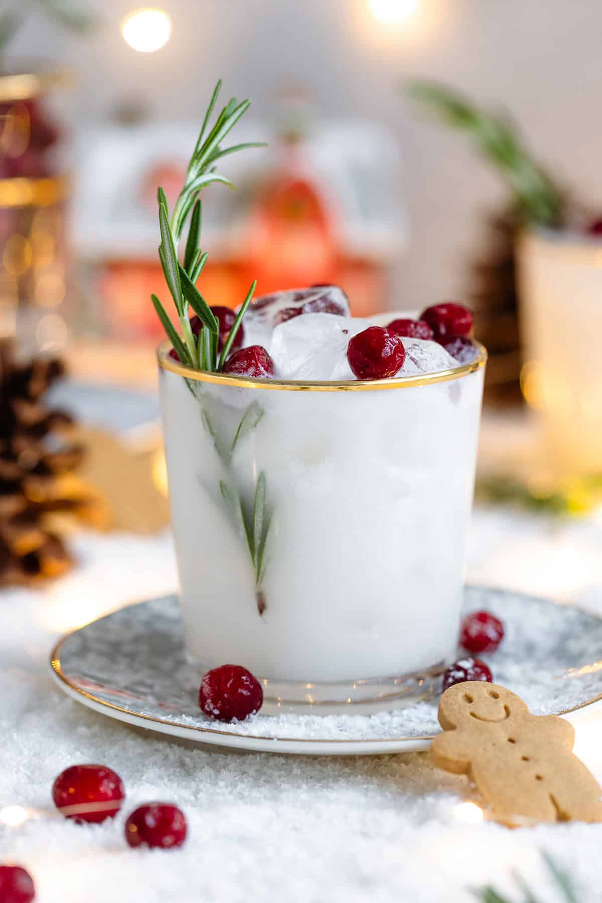 White margarita in a short glass with a gold rim, garnished with fresh cranberries, and rosemary spring.