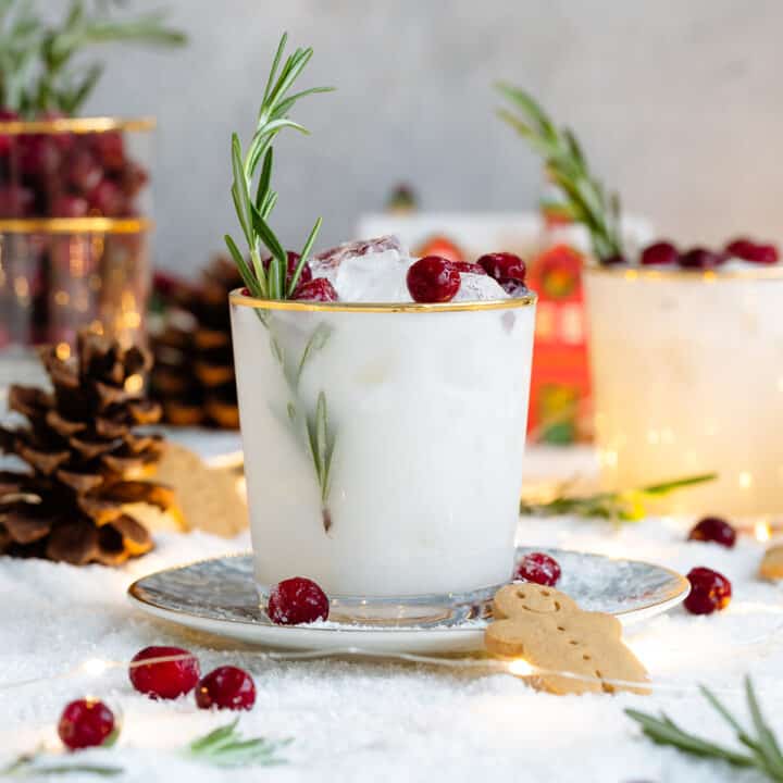 White margarita in a short glass with a gold rim, garnished with fresh cranberries, and rosemary spring.