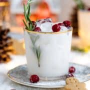 White margarita in a short glass with a gold rim, garnished with fresh cranberries, and rosemary spring.