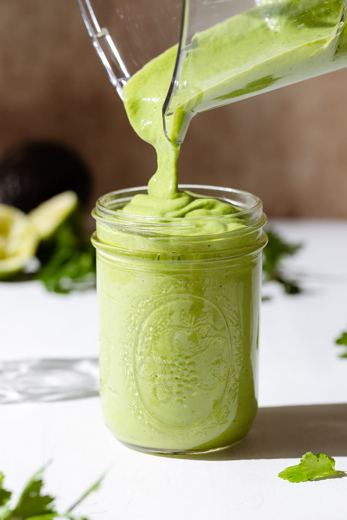 Thick green dressing being poured into a mason jar on a white background.