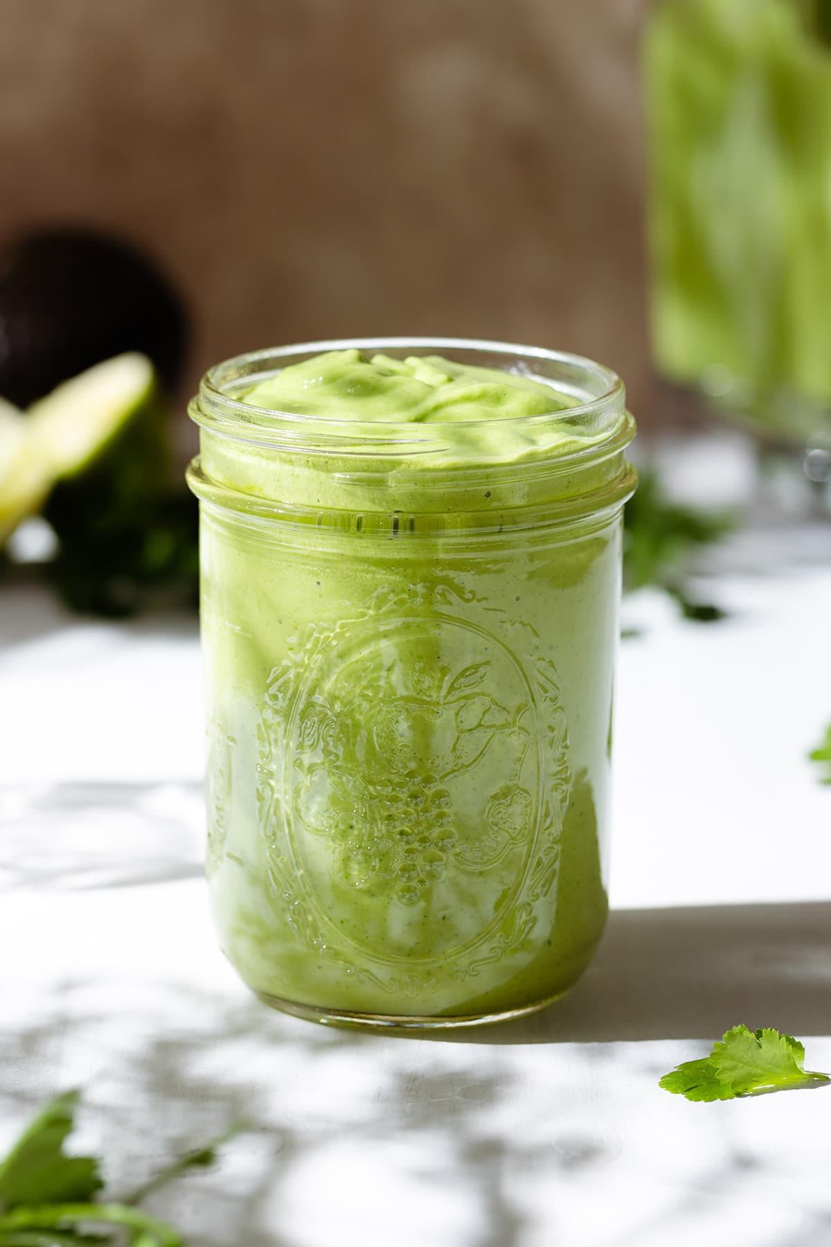 A mason jar with thick green dressing on a white background.