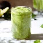A mason jar with thick green dressing on a white background.