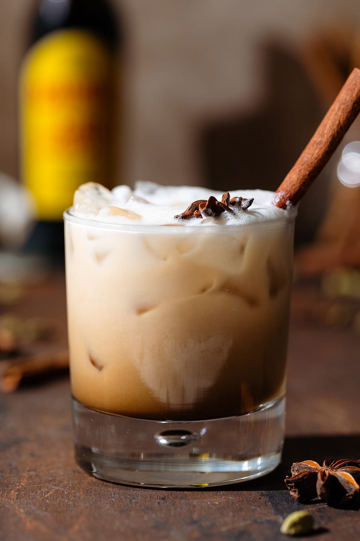 White Russian cocktail all mixed in a double old fashioned glass garnished with star anise on a wooden backdrop.
