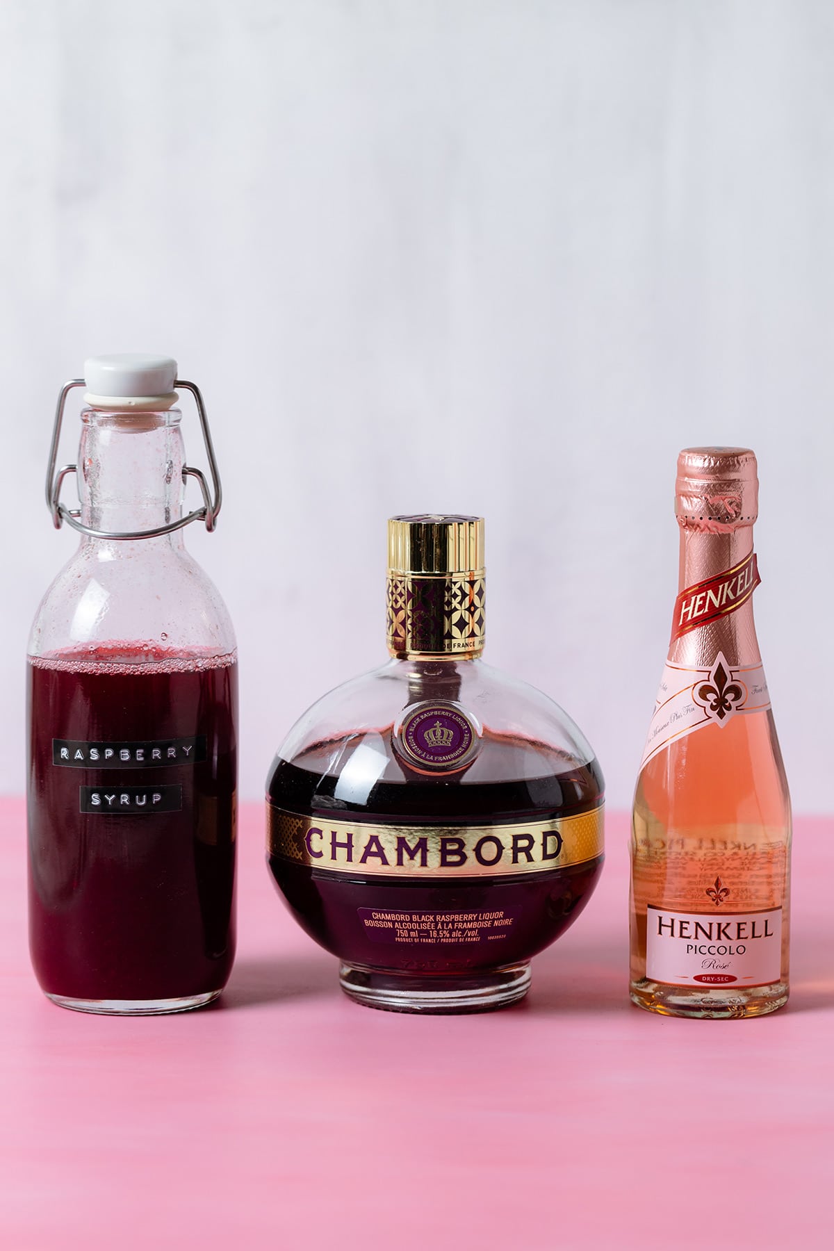 Raspberry syrup, Chambord, and Prosecco on pink and white background.