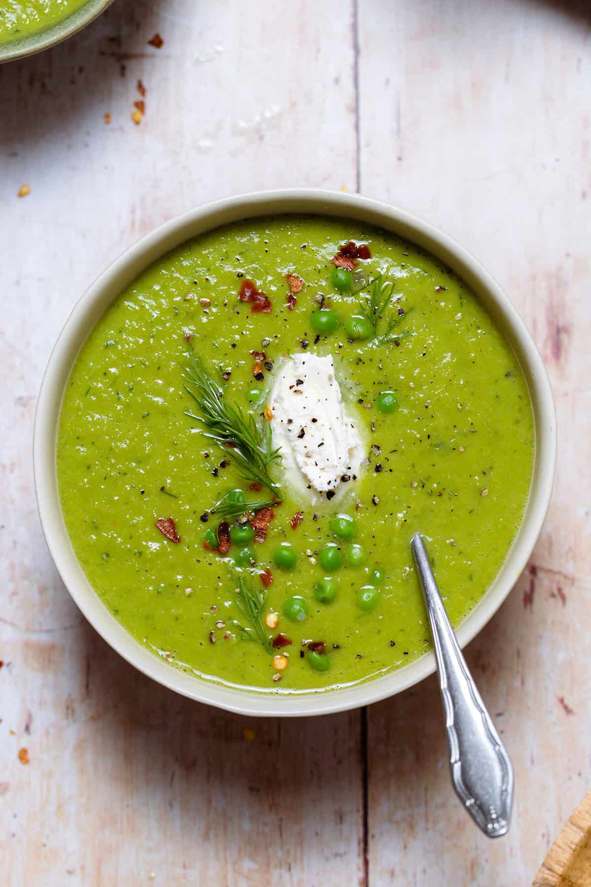 Green soup in white bowls on a light wooden background.