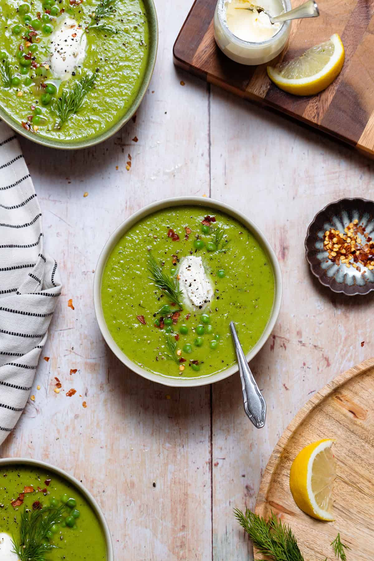 Green soup in white bowls on a light wooden background.