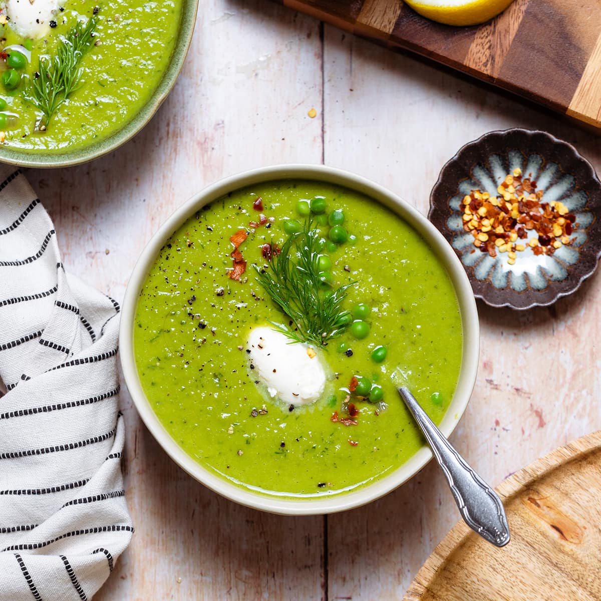 Green pea soup in white bowls on a light wooden backdrop.