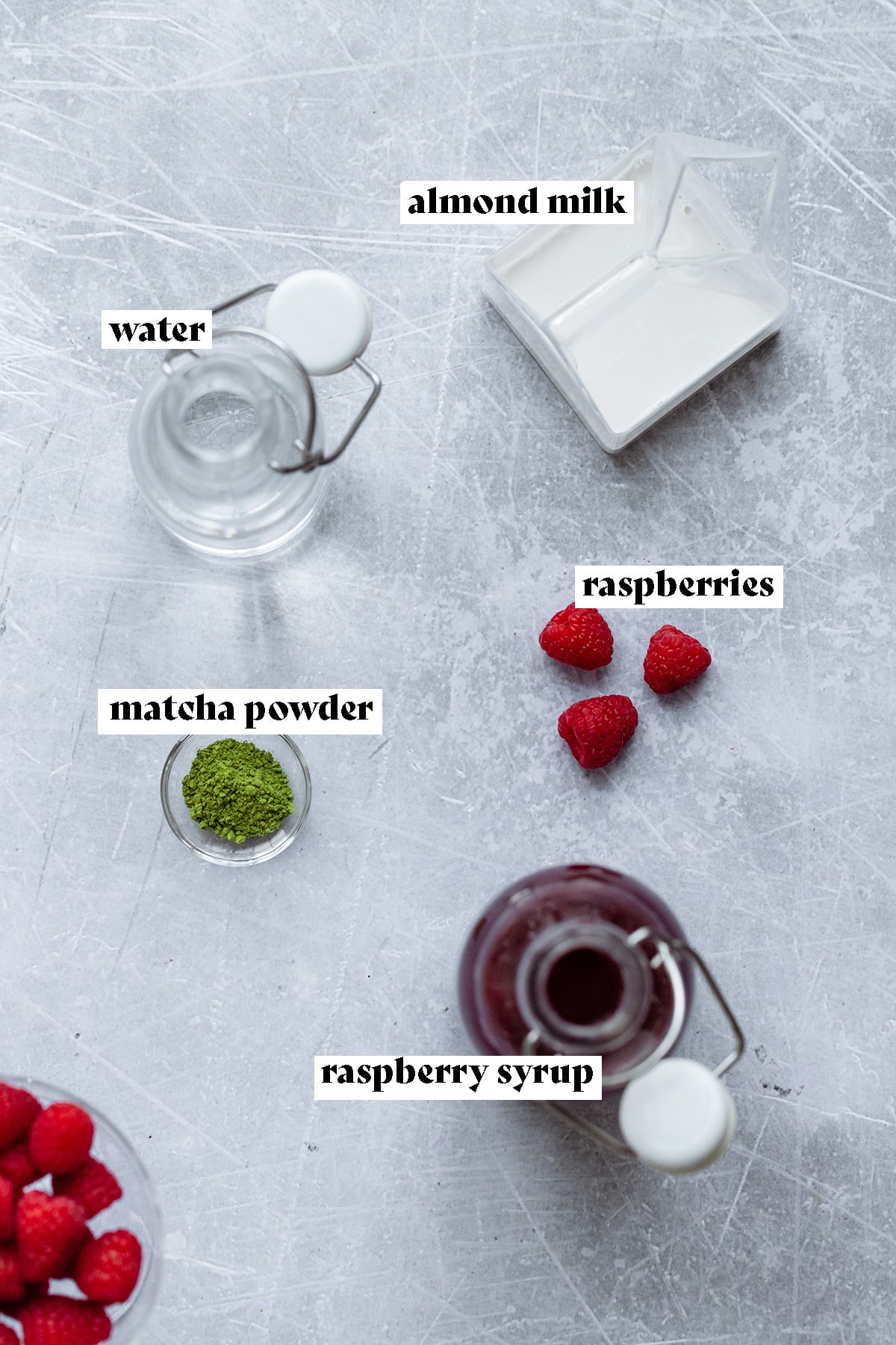 Raspberry syrup, raspberries, almond milk, water, and matcha powder on a metal background.