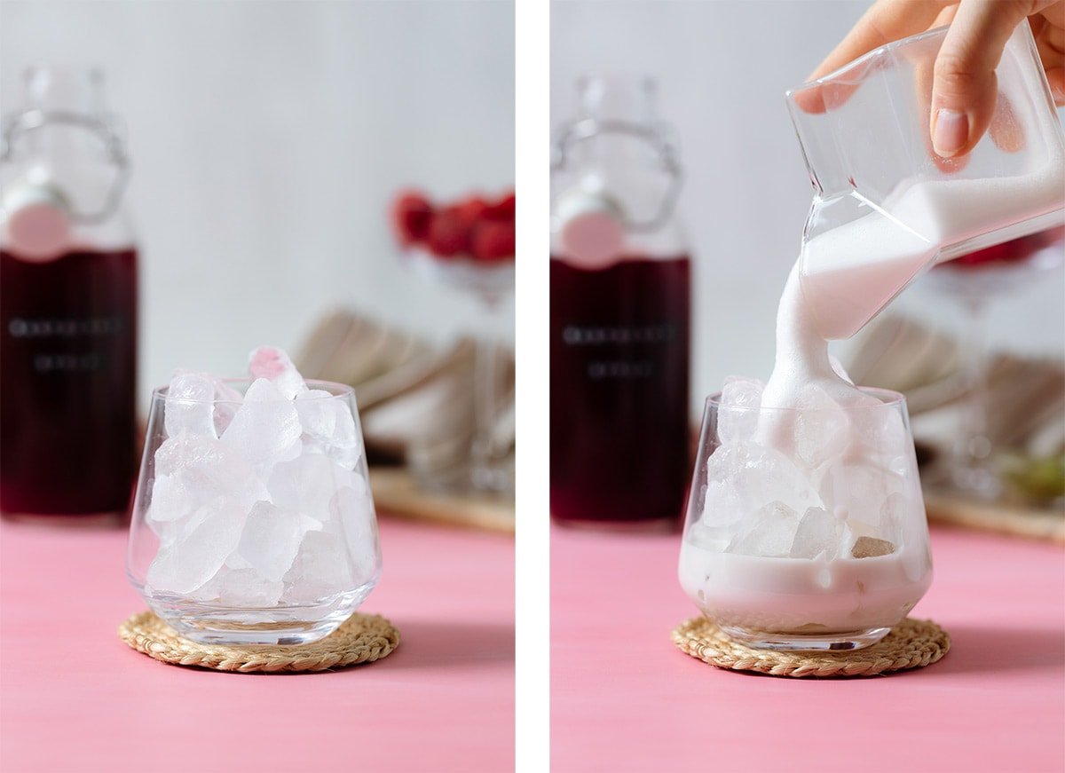 Almond milk being poured into a glass filled with ice on a pink and white background.