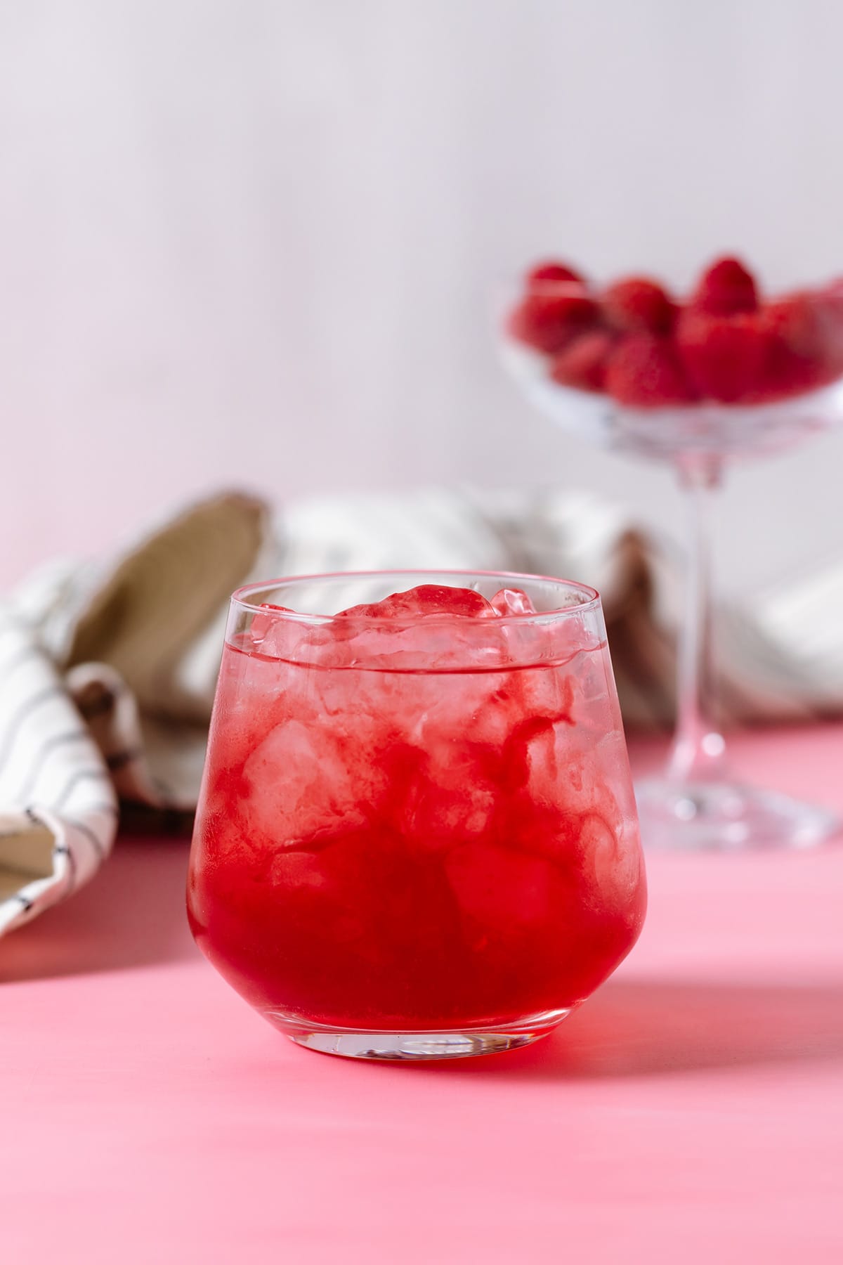 A glass with water and raspberry syrup on a pink and white background.