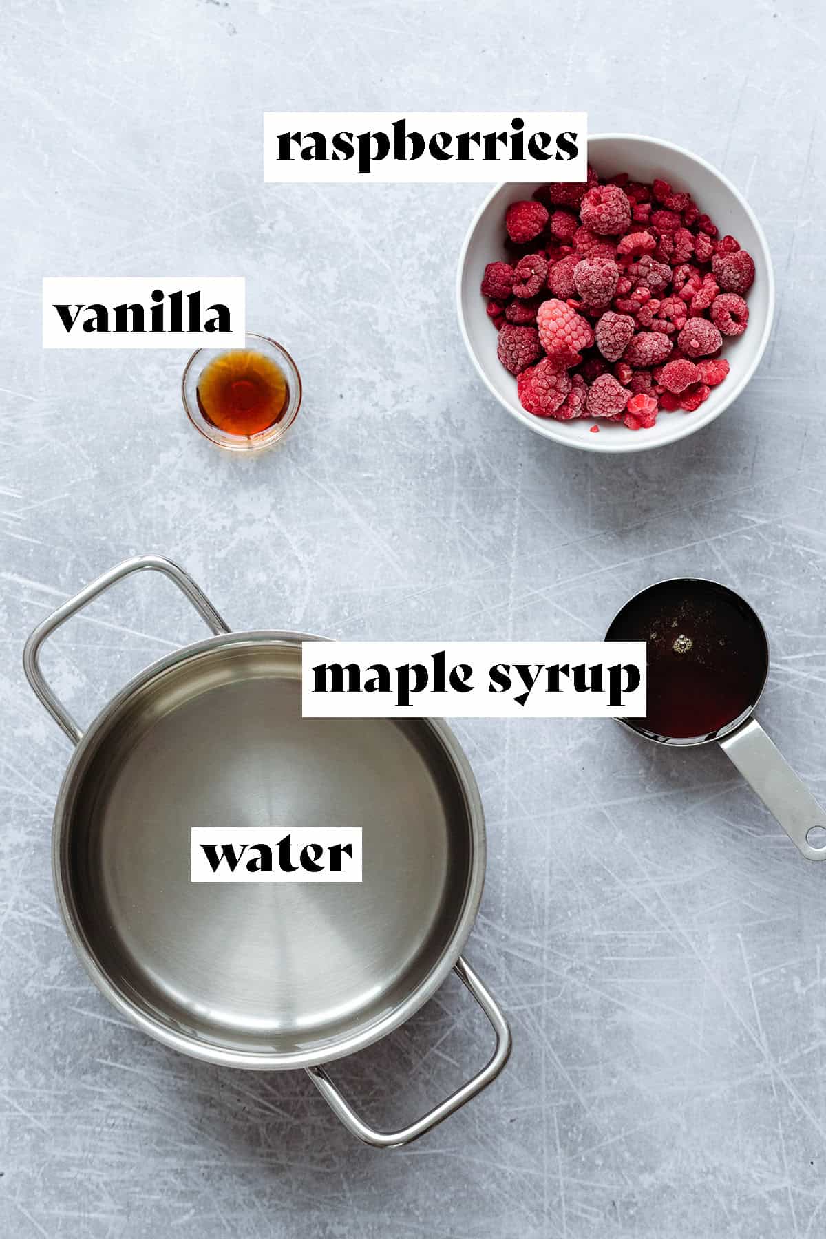 Water, maple syrup, raspberries, and vanilla laid out on a metal background.