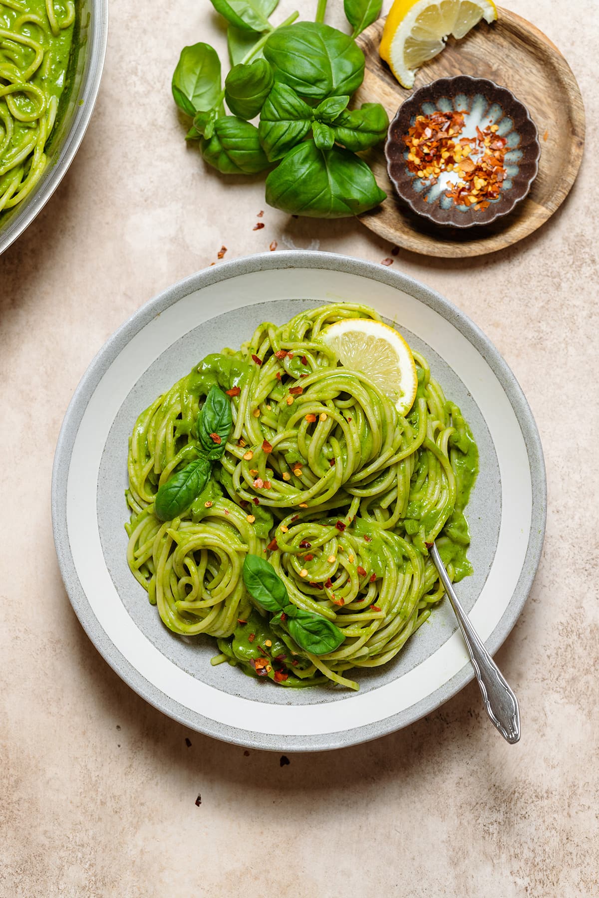 Spaghetti with green sauce in a low grey bowl garnished with fresh basil, chili flakes, and lemon.