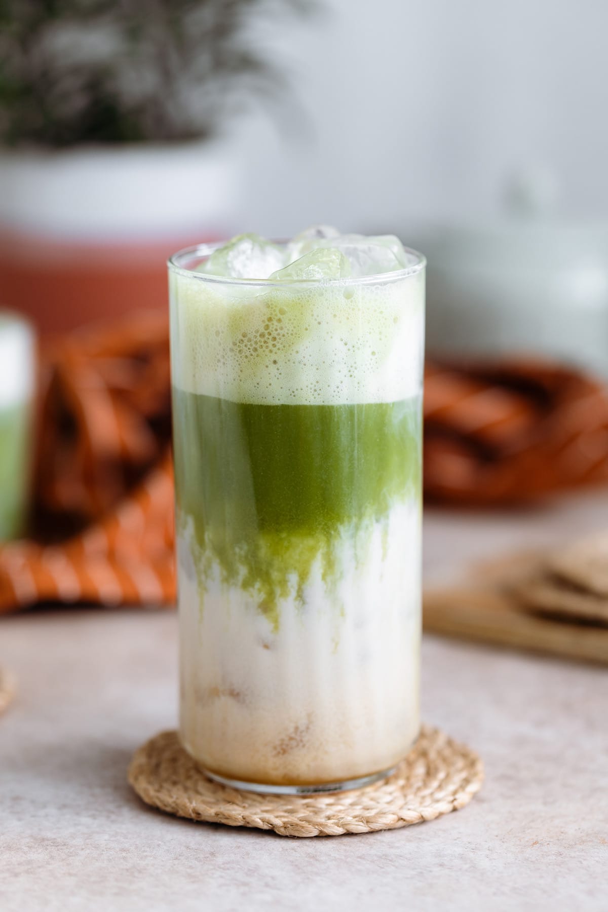 Matcha latte in a tall glass with a glass straw,matcha is floating on top of the milk.