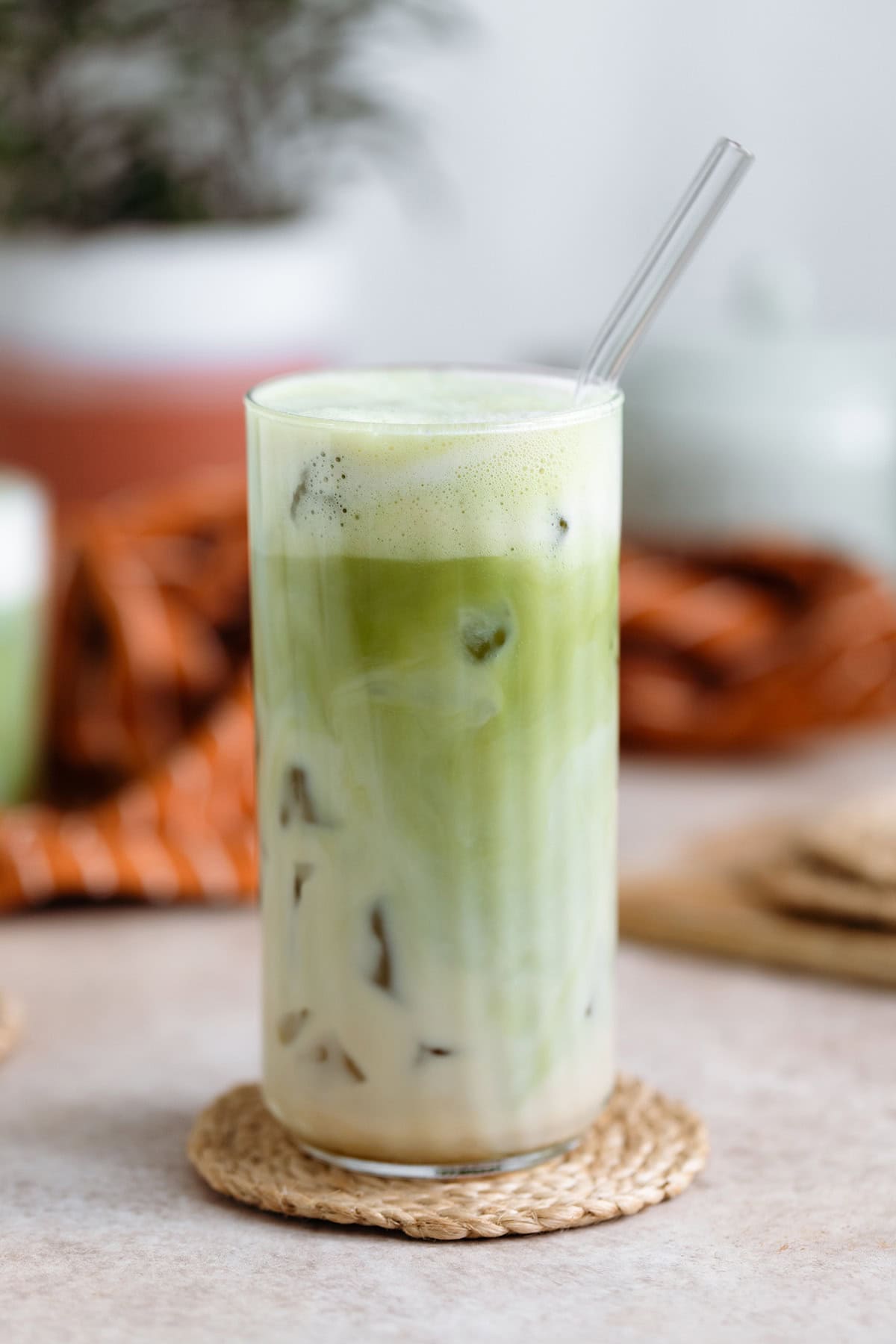 Matcha latte in a tall glass with a glass straw on light beige background.