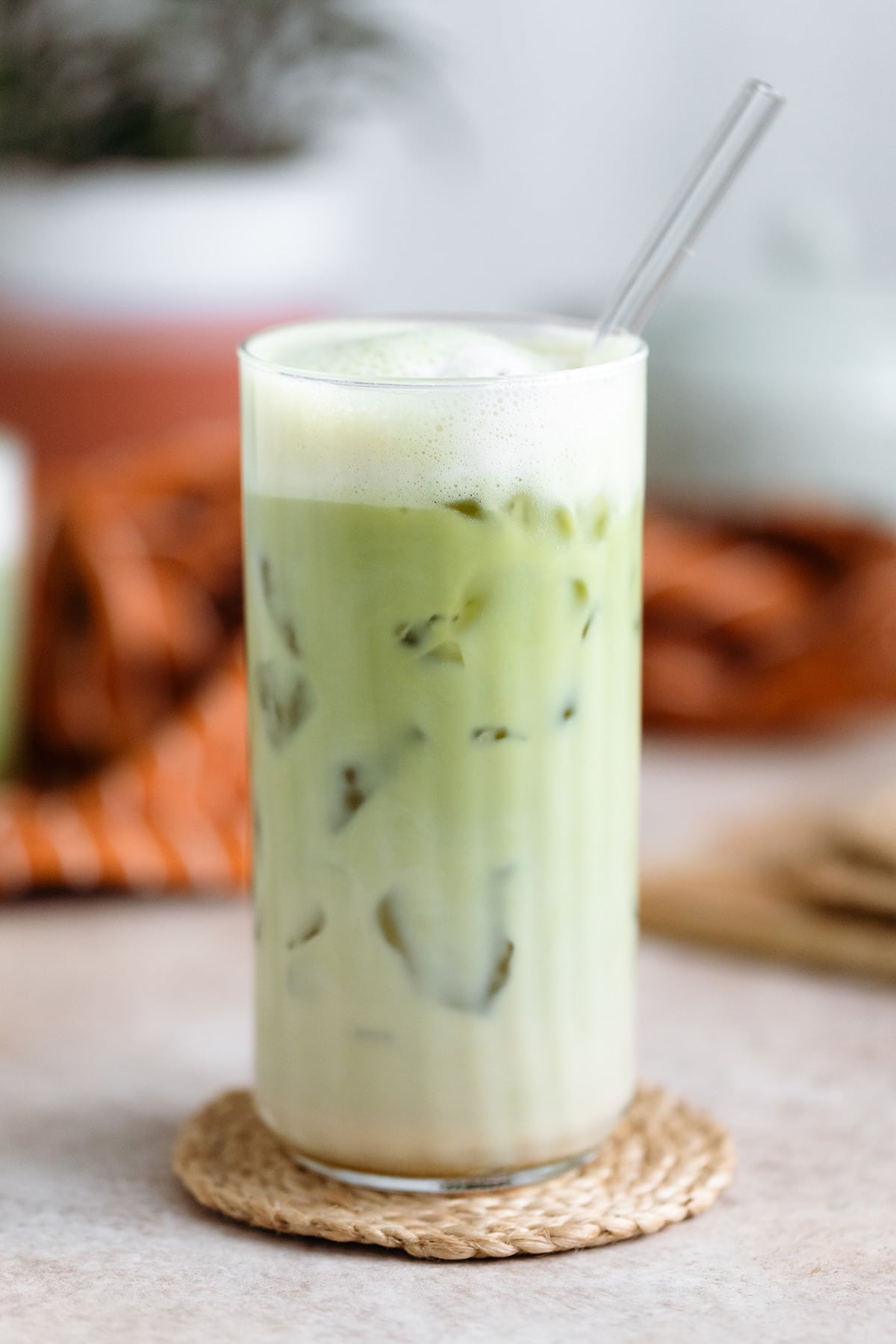 Matcha latte in a tall glass with a glass straw on light beige background.