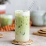 Matcha latte in a tall glass with a glass straw on light beige background.