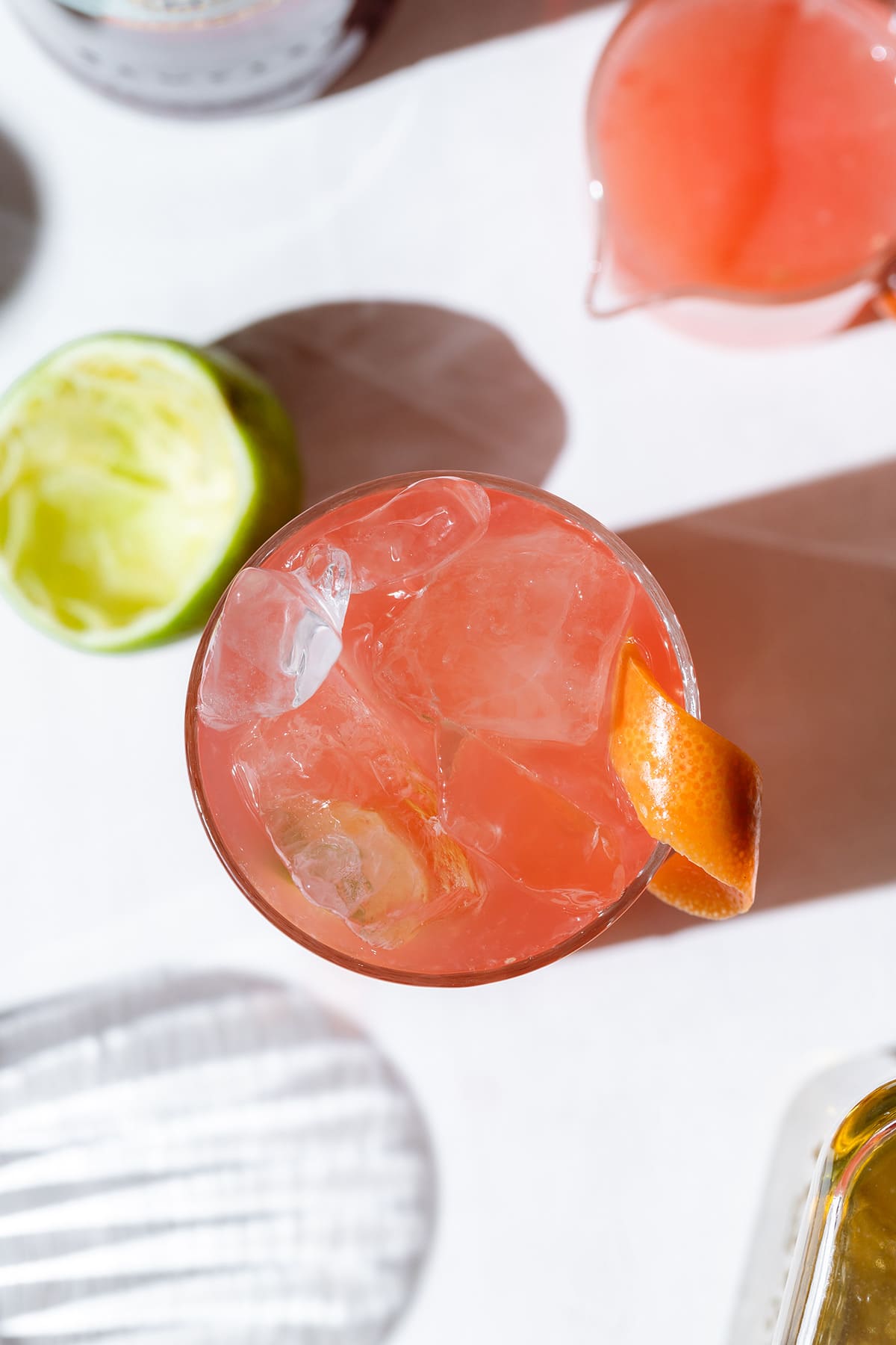 Overhead shot of peach colored campari cocktail in a glass with ice and an orange peel.