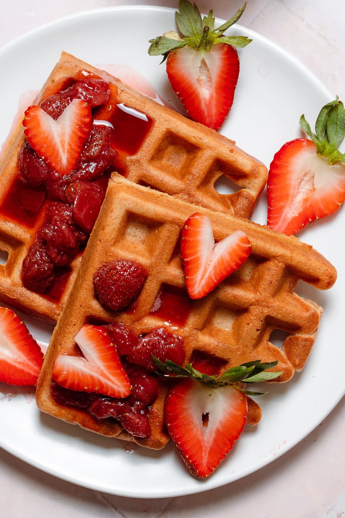 Waffles with syrup and fresh strawberries on a white plate on a stone background.