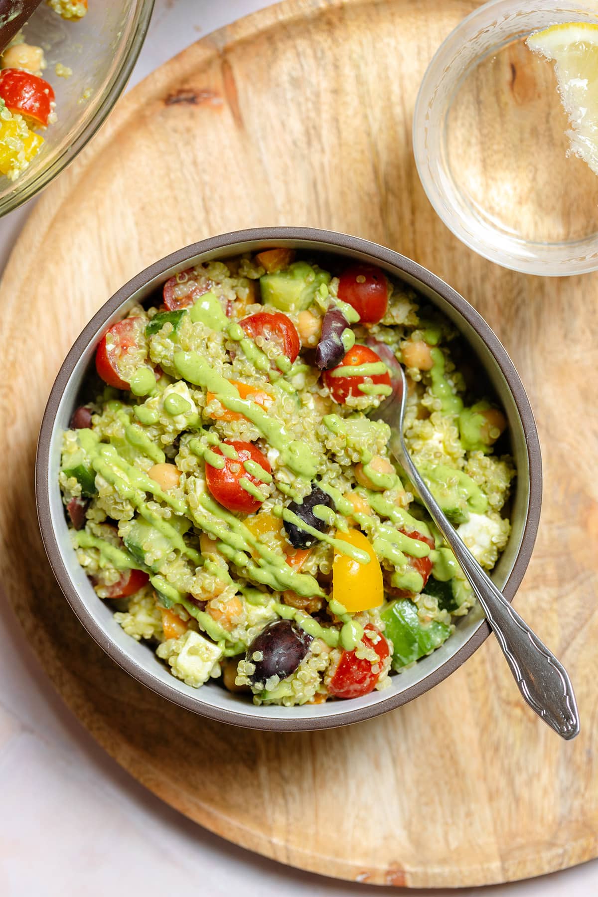 Colorful vegetable quinoa salad with green avocado dressing in a ceramic bowl on a wooden serving plate.